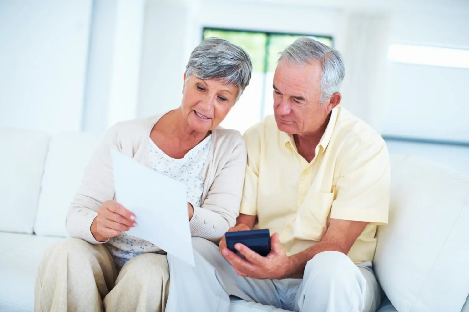 An older couple on a sofa checking a letter and a calculator together